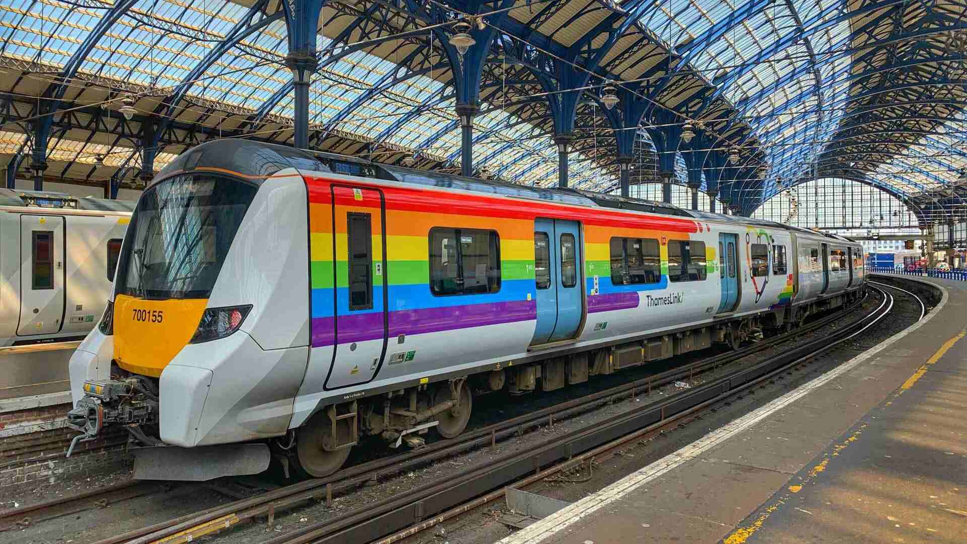 A rainbow coloured train sitting at a platform in Brighton station
