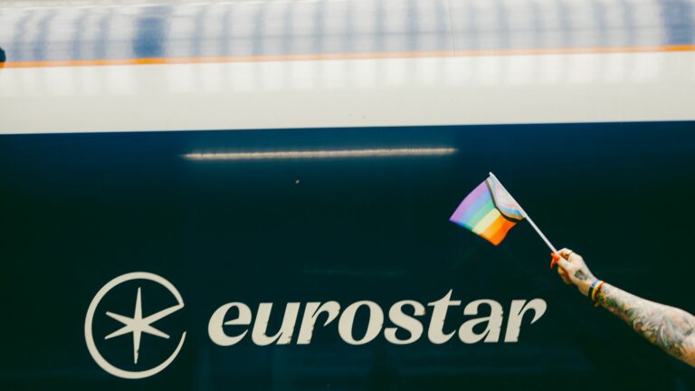 A hand holding a Progress Pride flag in front of a Eurostar train.