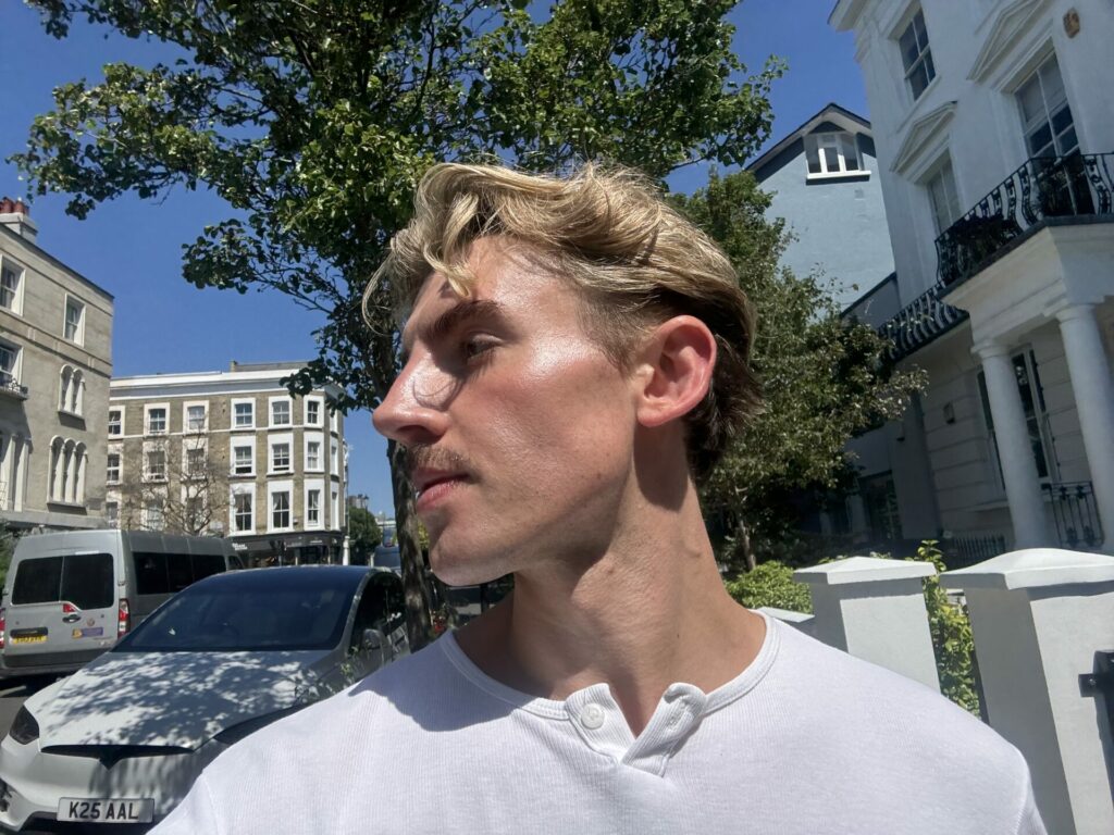 Jacob Seickell with a city backdrop, his skin shining in the sun wearing a white t-shirt