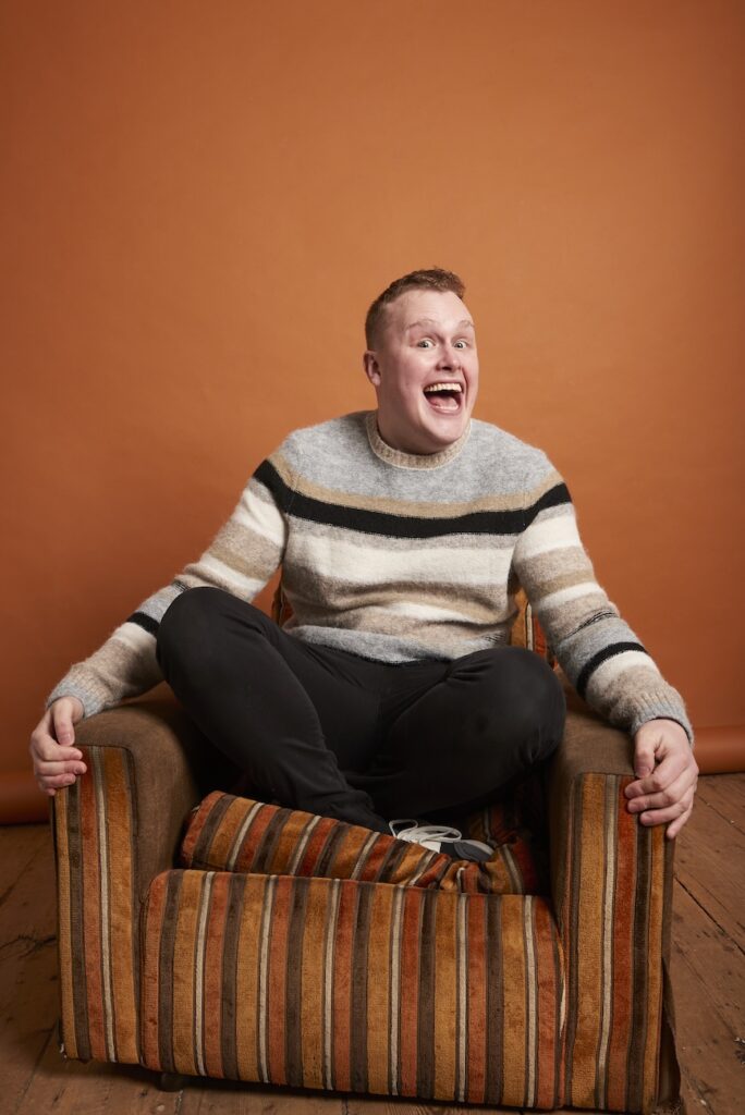 josh jones in a white striped jumper sat on an orange sofa chair