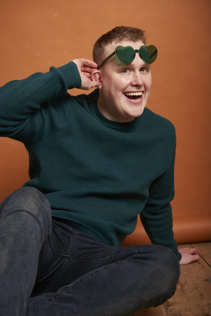 Josh in sunglasses that he's pulling up, green jumper and orange colourama