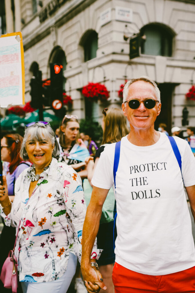 Elderly man wearing a 'protect the dolls' t-shirt holding hands with an elderly woman at London Trans+ Pride 2025