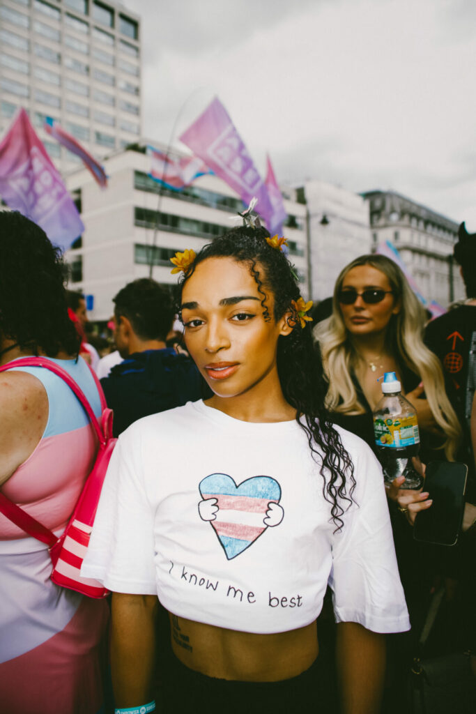 Alex Thomas-Smith with yellow flowers in their hair and a white t-shirt with a heart coloured blue, pink and white with the words 'I know me best' written below it