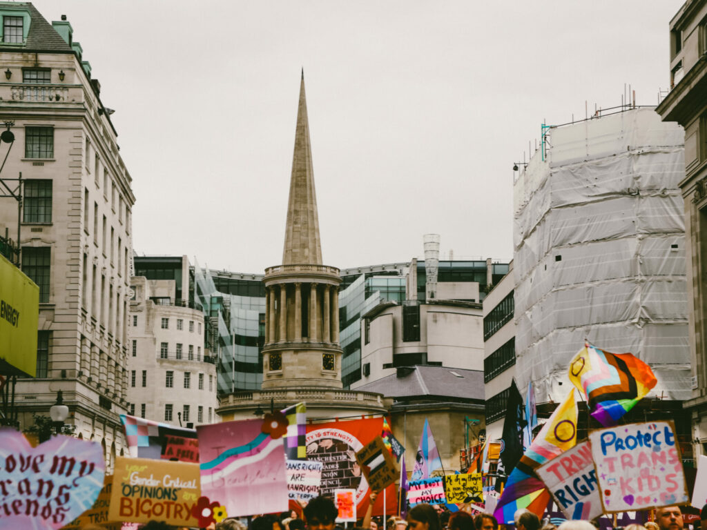 A river of banners and signs protesting for trans rights as well as rainbow and trans flags raised high about them