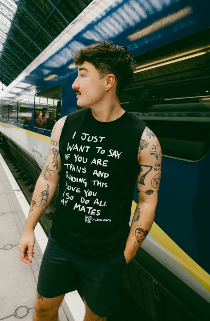 A man with tattooed arms in a sleeveless vest standing in front of a Eurostar
