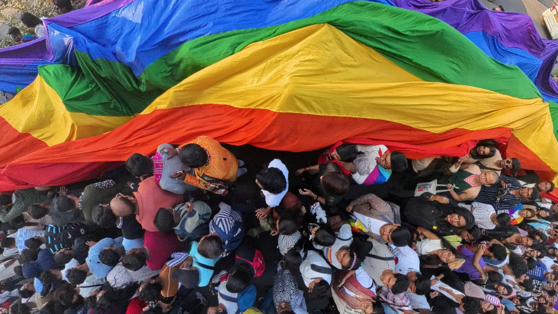Pride parade of people holding a pride flag above their heads