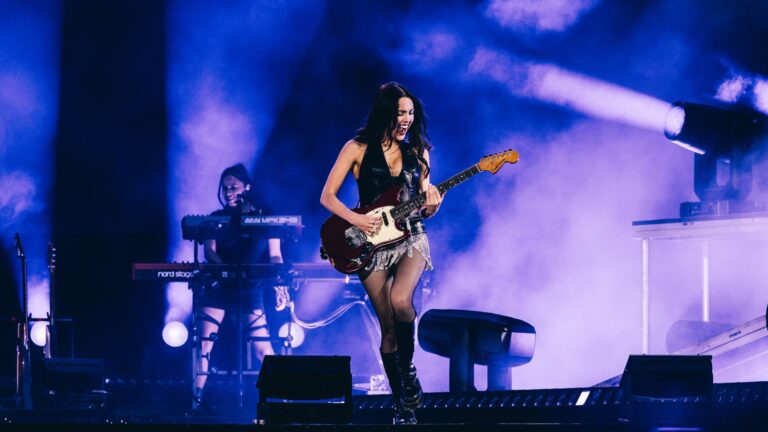 Olivia Rodrigo on stage in black top and silver skirt playing guitar