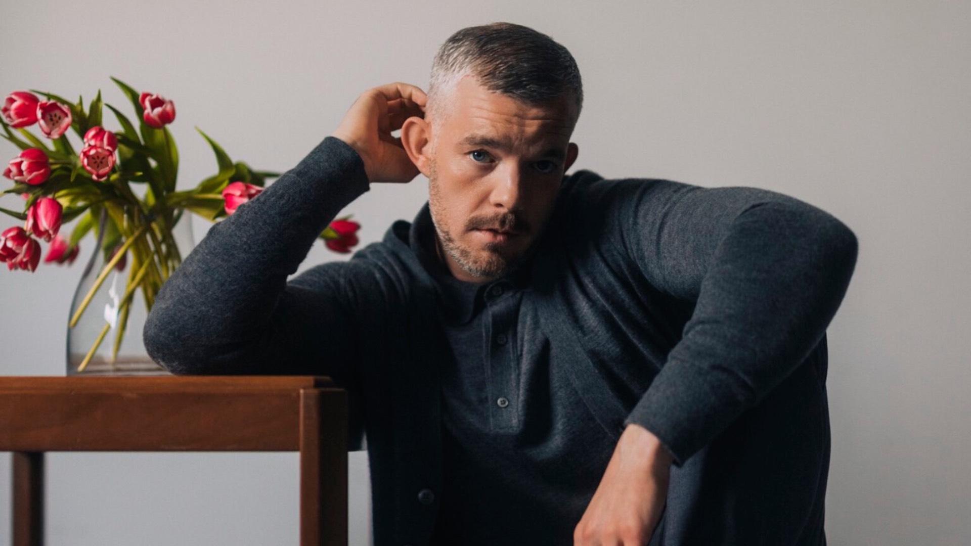 Russell Tovey in grey top with flowers behind him (Image: Rolling Stone UK)