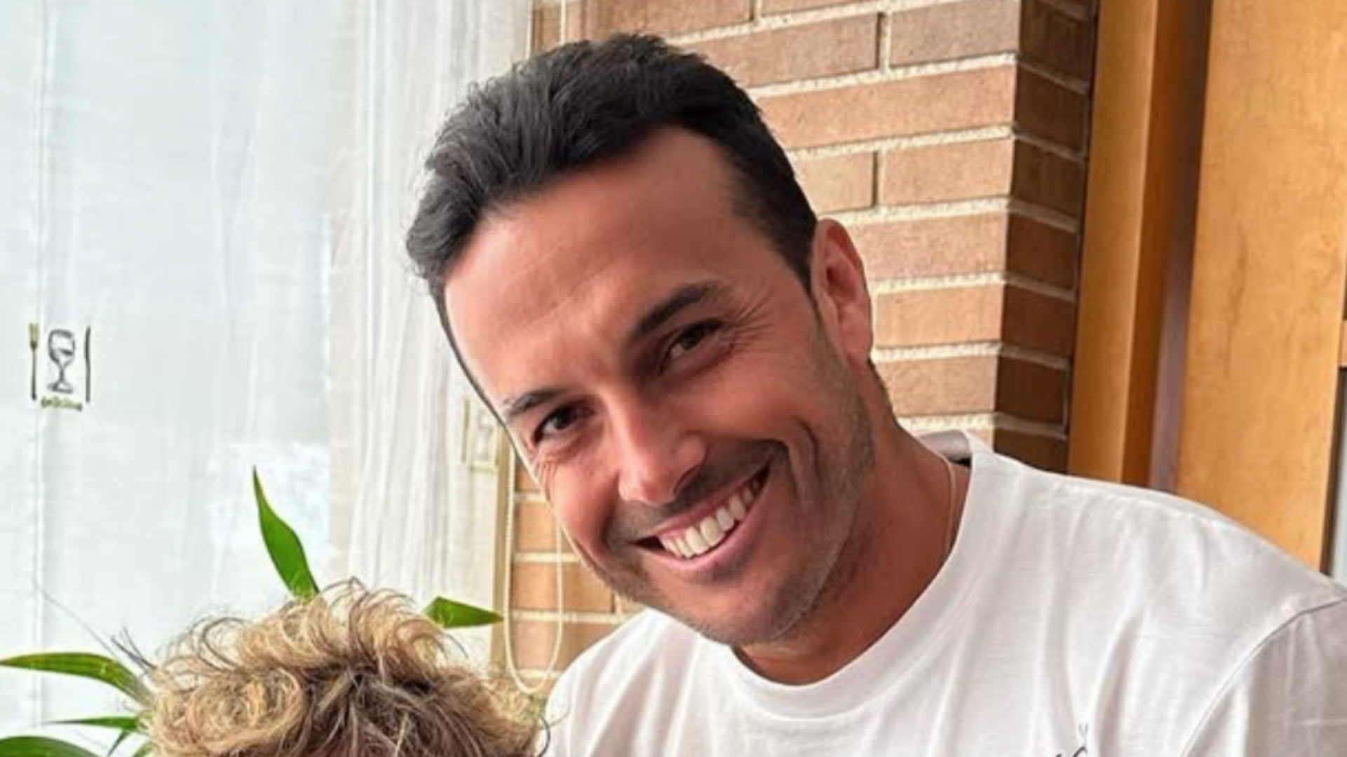 Pedro Rodríguez in a white t-short smiling in front of a brick wall