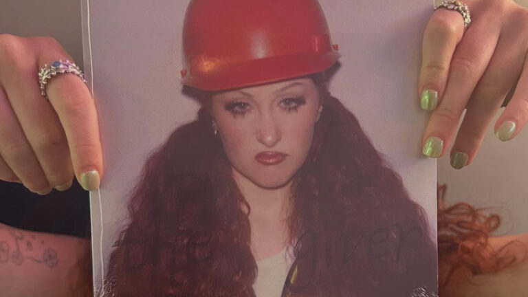 Chappell Roan holding up 'The Giver' artwork of her wearing a red builders hat