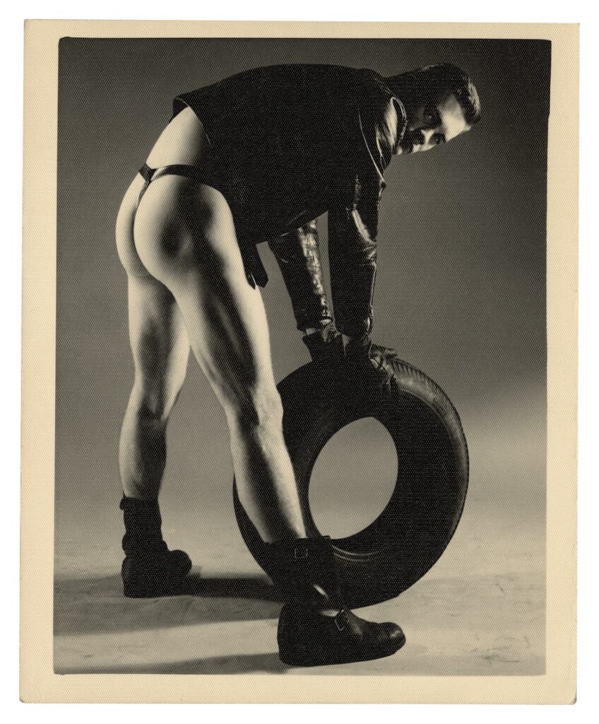 a man in a black leather jacket and a black leather thong rolling a tyre
