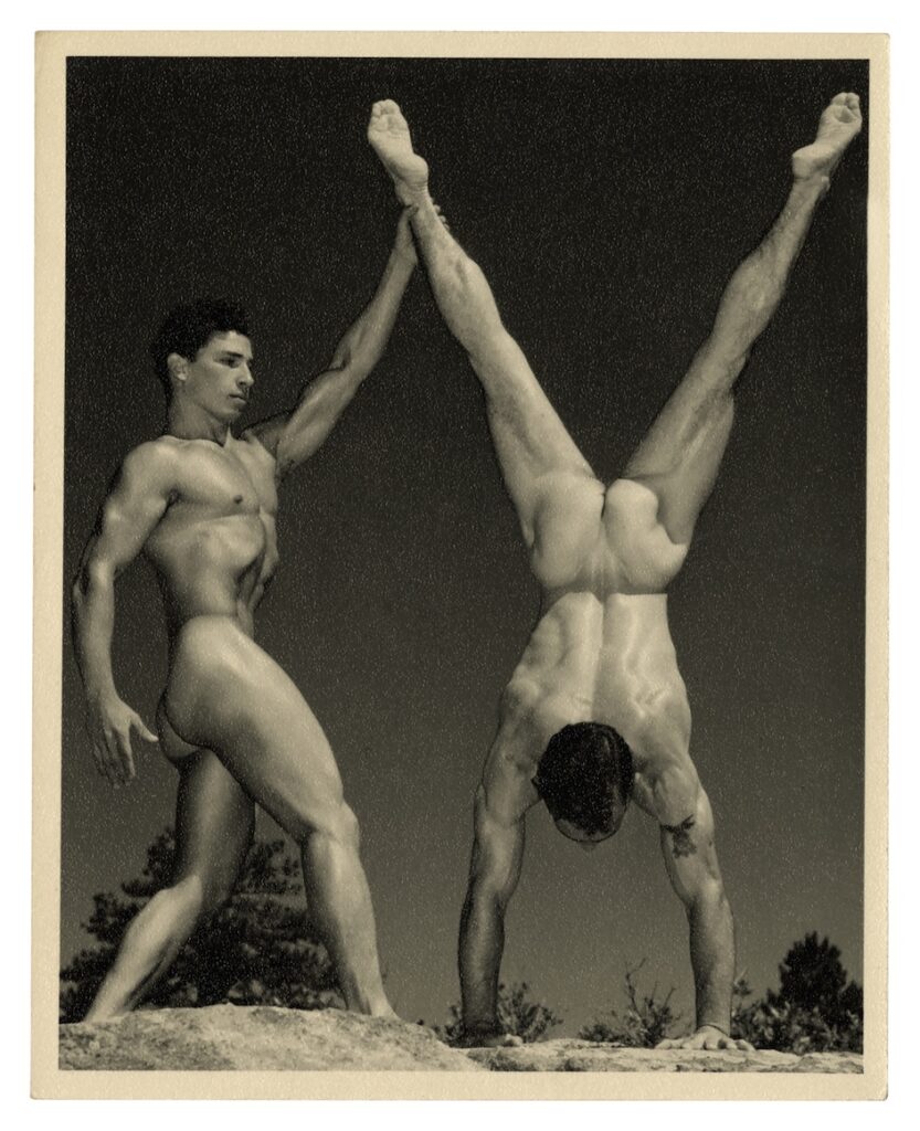 two men naked, one doing a handstand and the other holding his foot