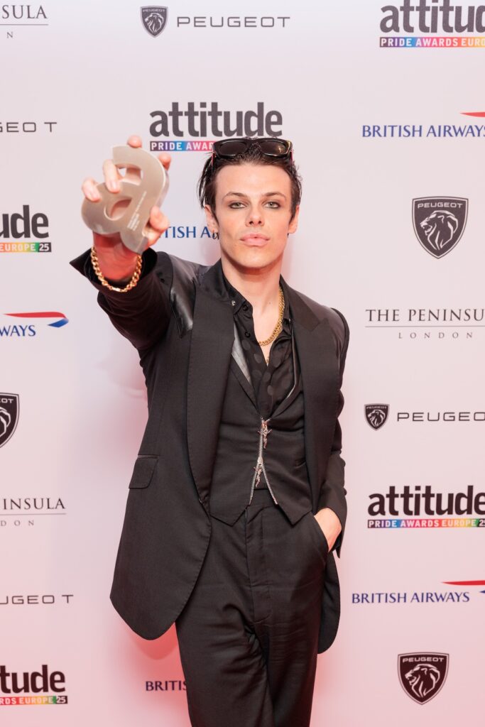 yungblud in black suit on red carpet holding up attitude award