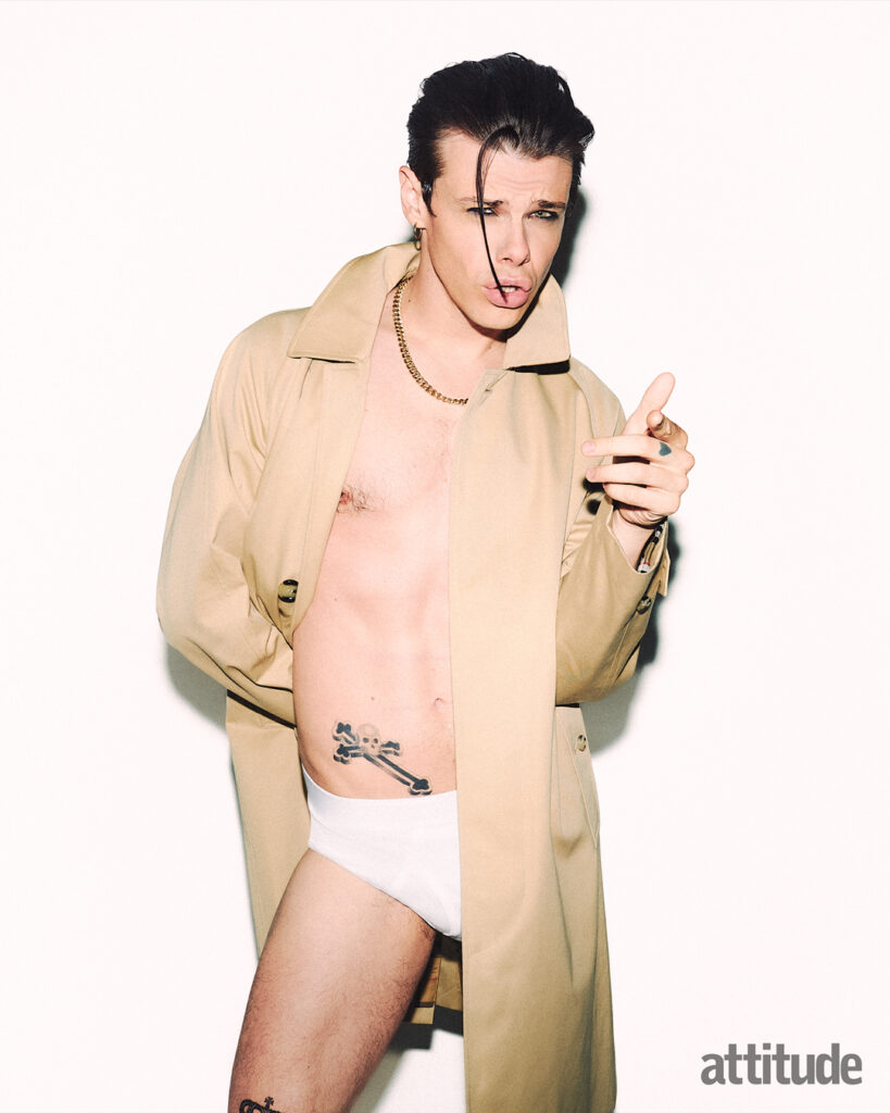 yungblud pulling open a tan coat, with nothing on underneath but a pair of white underwear