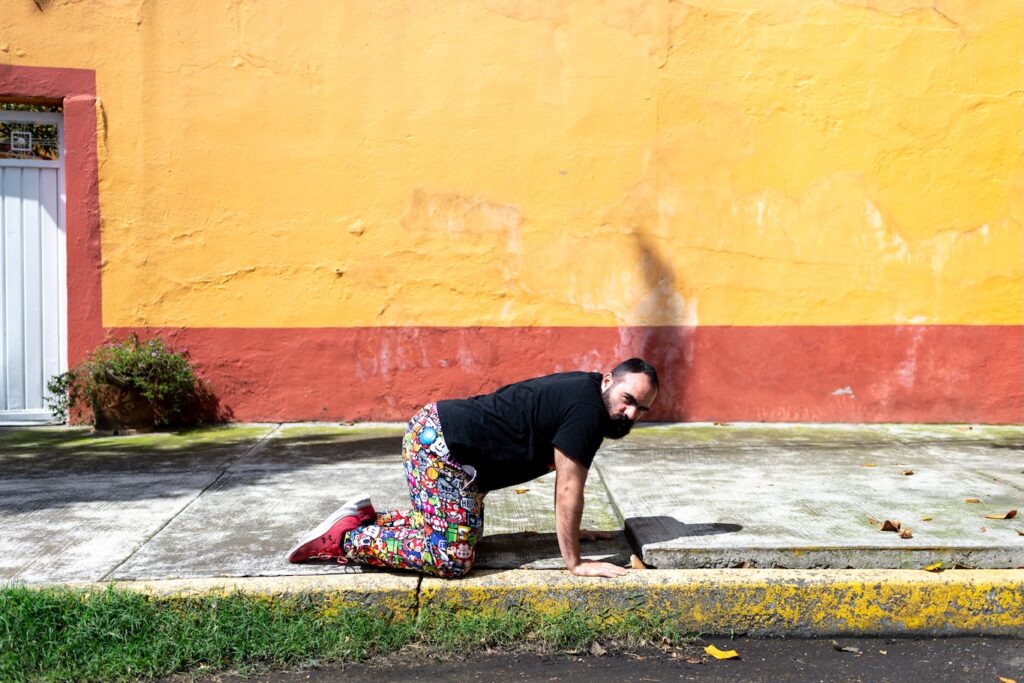 Jalil M crawling down street, yellow wall behind
