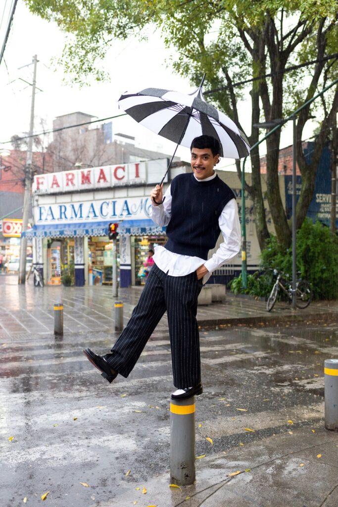 Fernando G in pinstripe trousers, white shirt and waistcoat, holding an umbrella in the rain