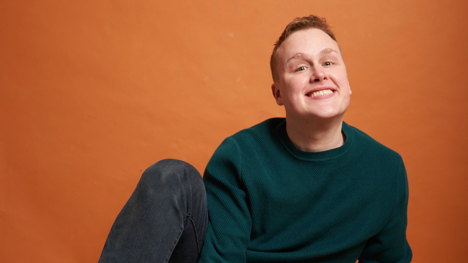 Josh Jones in black top against orange background (Image: Josh Faithi)