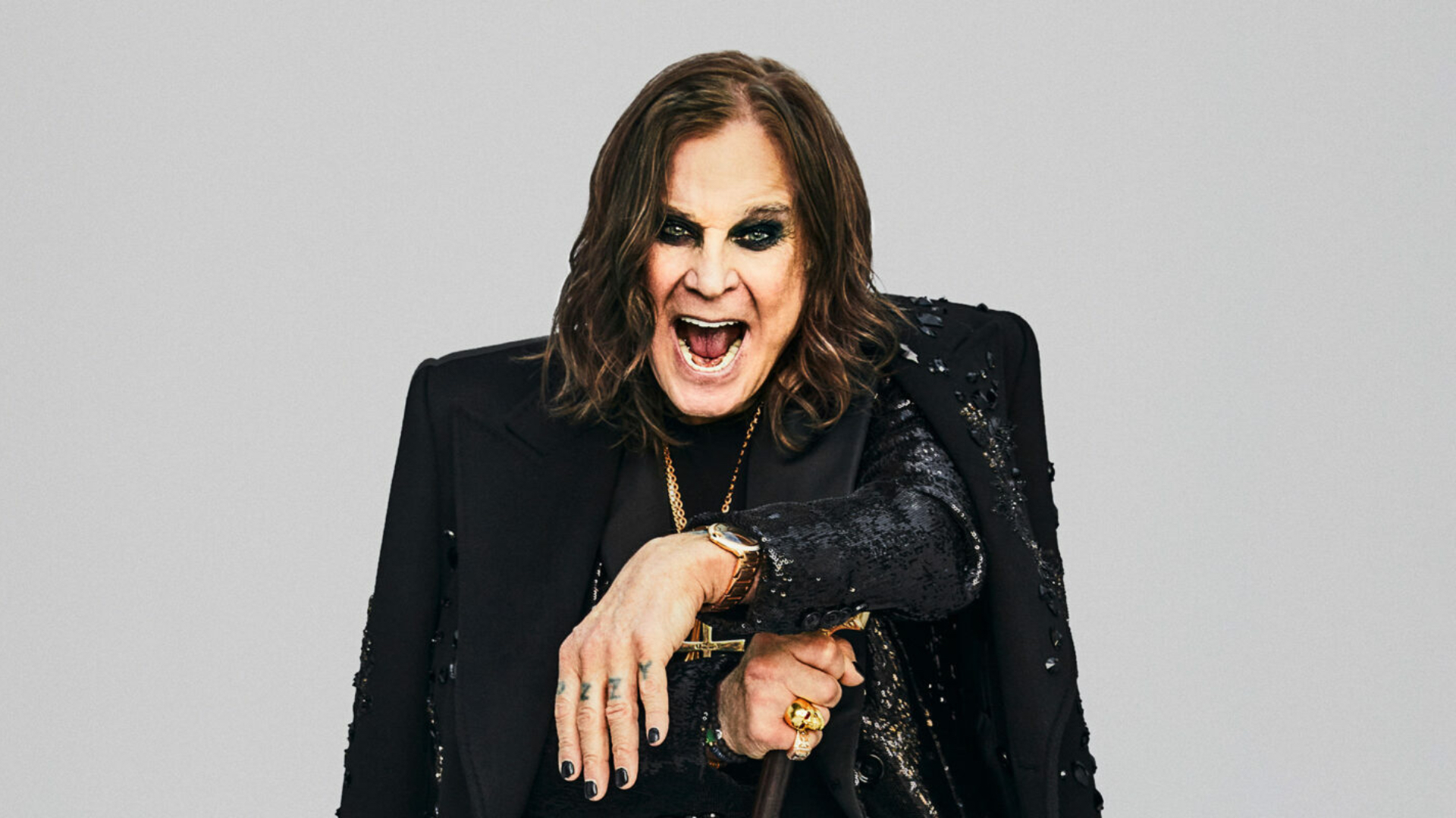 Ozzy wears shirt, trousers, coat and overcoat by Dolce & Gabbana, necklaces by Chrome Hearts, rings by Rockford Collection, bracelets by Luis Morais, watch by Cartier, holding cane by fashionable canes