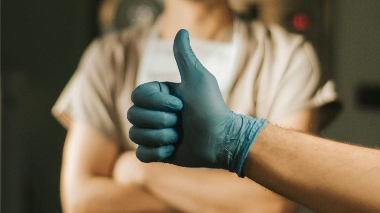 A doctor putting their thumbs up wearing a rubber glove