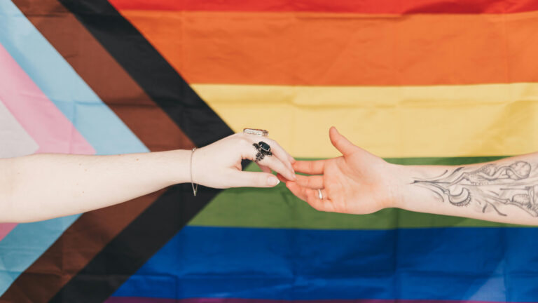 hands touching in front of a pride flag