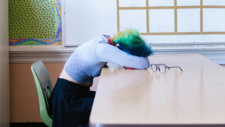 Student with rainbow coloured hair with their head down on the desk