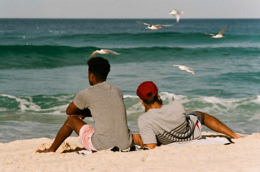 Two men lying on a beach facing the ocean