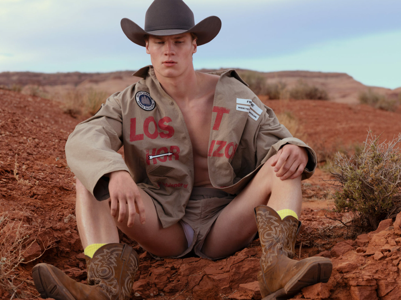 Against the Utah desert sits a model wearing a cowboy hat, cowboy boots, and an undone shirt from Snow Goose by Canada Goose Spring/Summer 2025 collection.