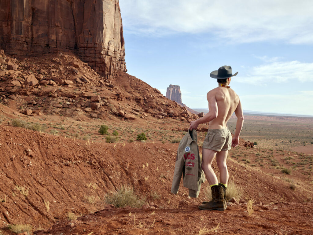 Against the Utah desert sits a shirtless model holds onto a utilitarian shirt from the Snow Goose by Canada Goose Spring/Summer 2025 collection.