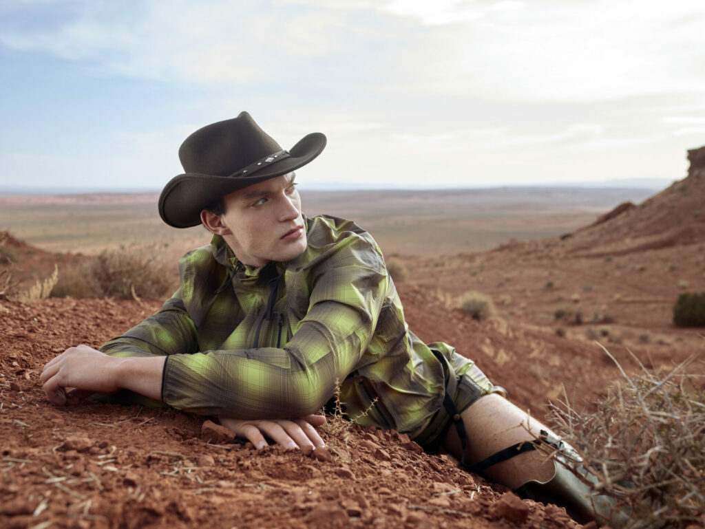 Against the Utah desert sits a model wearing a cowboy hat, cowboy boots, and a plaid shirt from Snow Goose by Canada Goose Spring/Summer 2025 collection.