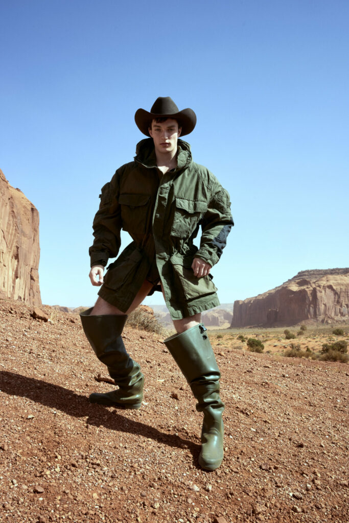 A model wearing a green jacket and green hat and boots posing in the Utah desert