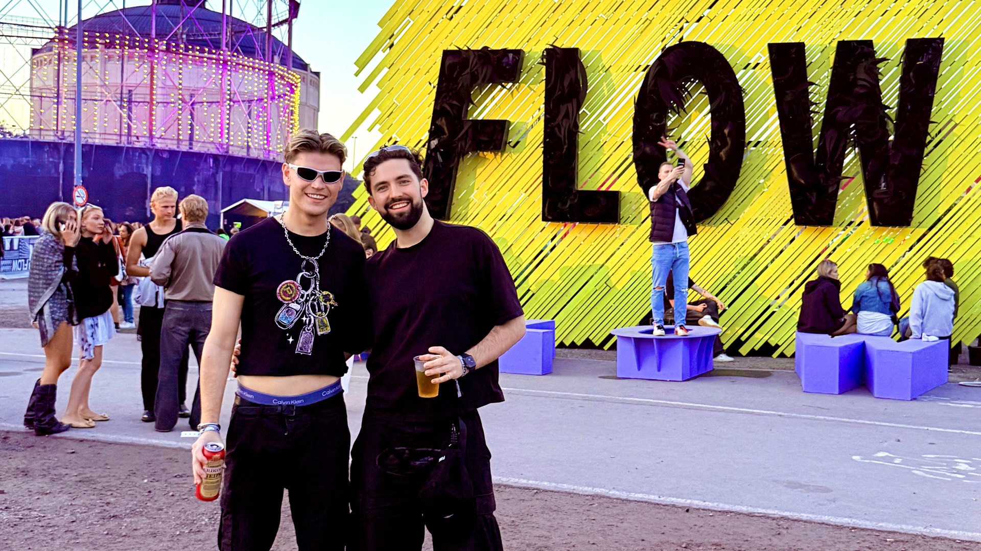 Attitude's Ashley Davey (left) at Flow Festival standing with a friend both in black with Flow mural in background