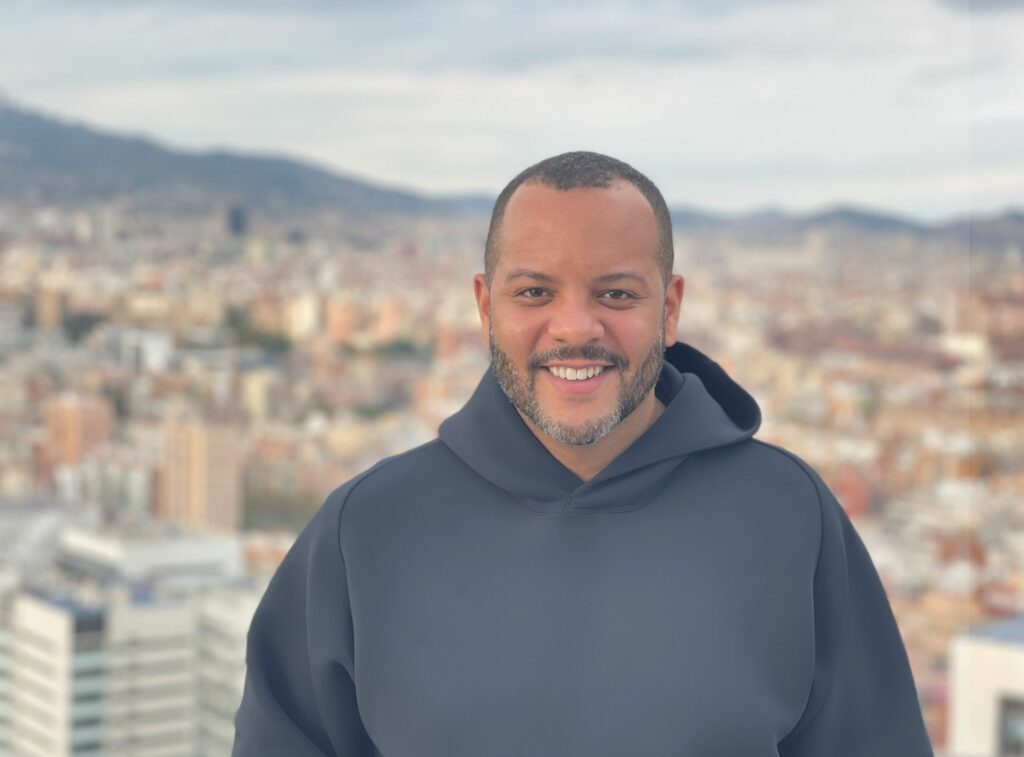 A smiling man wearing a black hoodie standing in front of a cityscape
