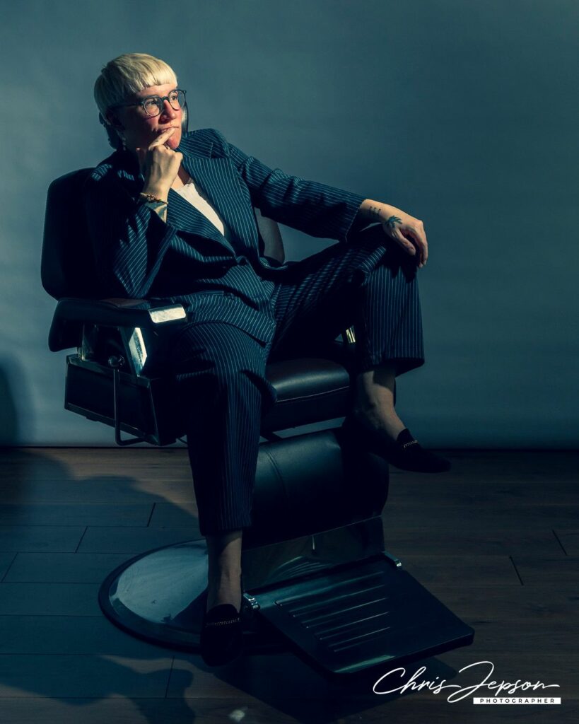 A person wearing a black suit sitting in a barber's chair