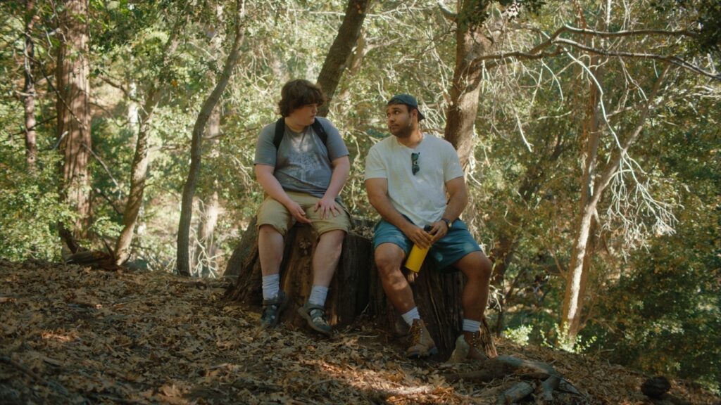 Isaac Krasner and David Johnson II sat on a tree stump looking at each other in the woods