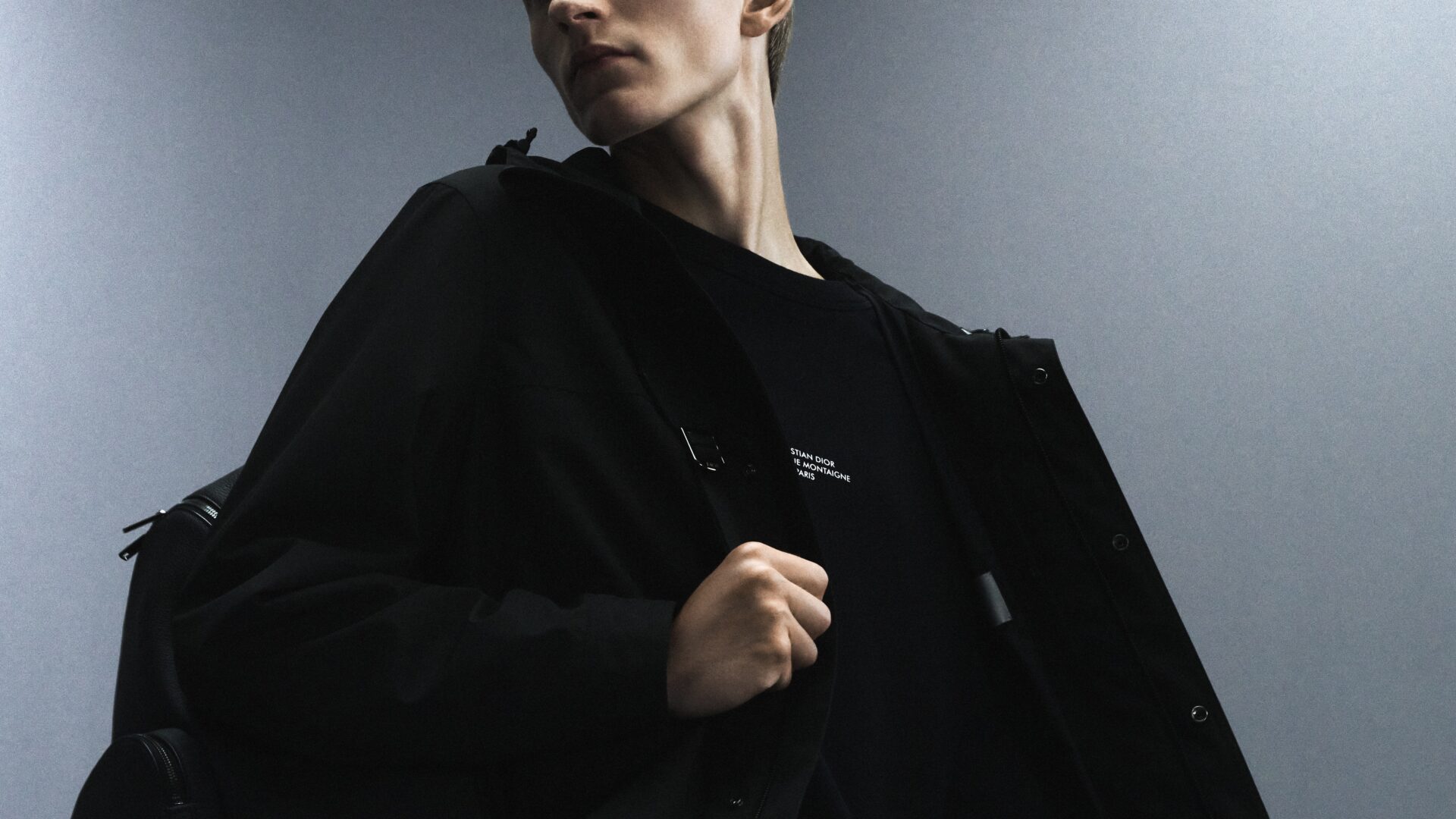 Close-up of a model wearing all black jacket and rucksack from the Dior Men's "Back in Town" capsule collection