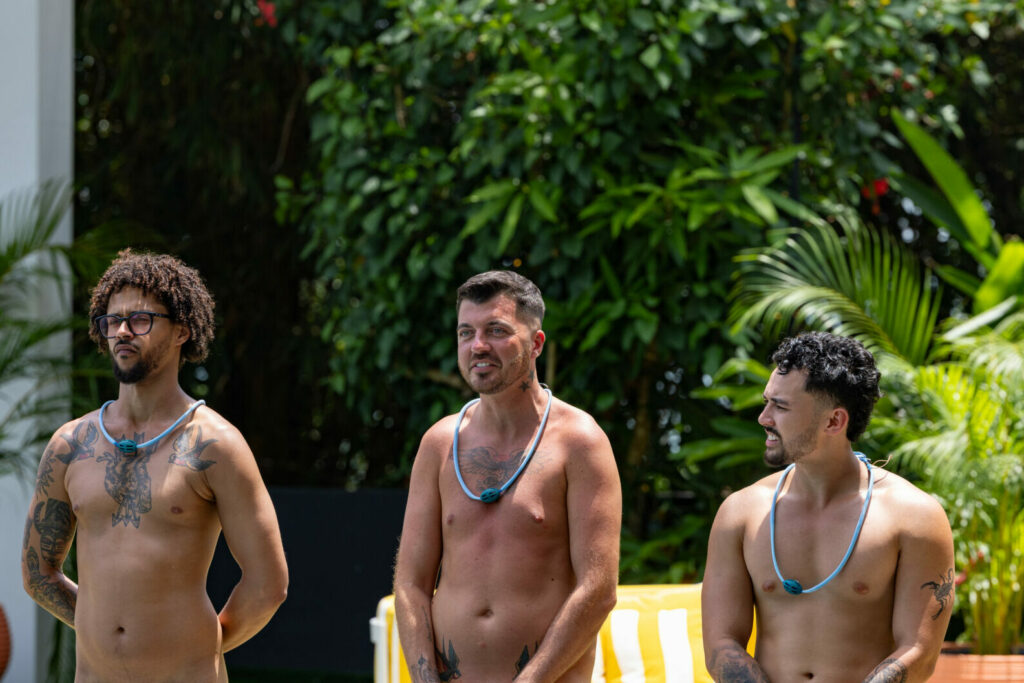 Three topless men in front of a green natural backdrop