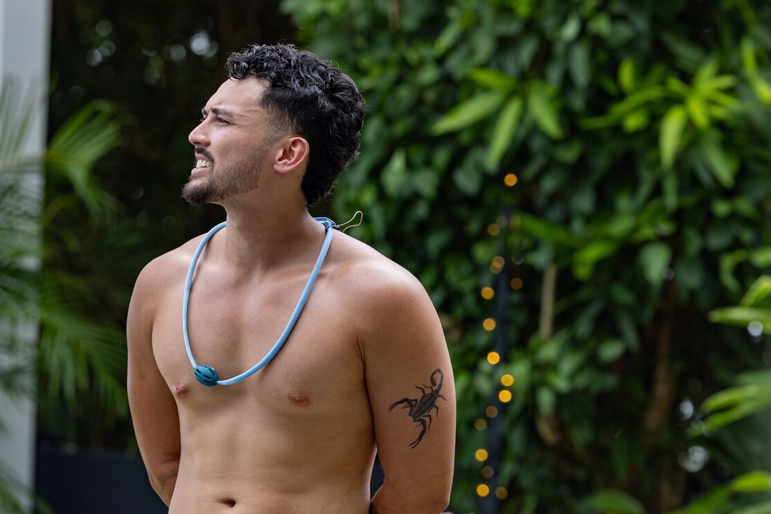 Topless man smiling to the left in front of a bush