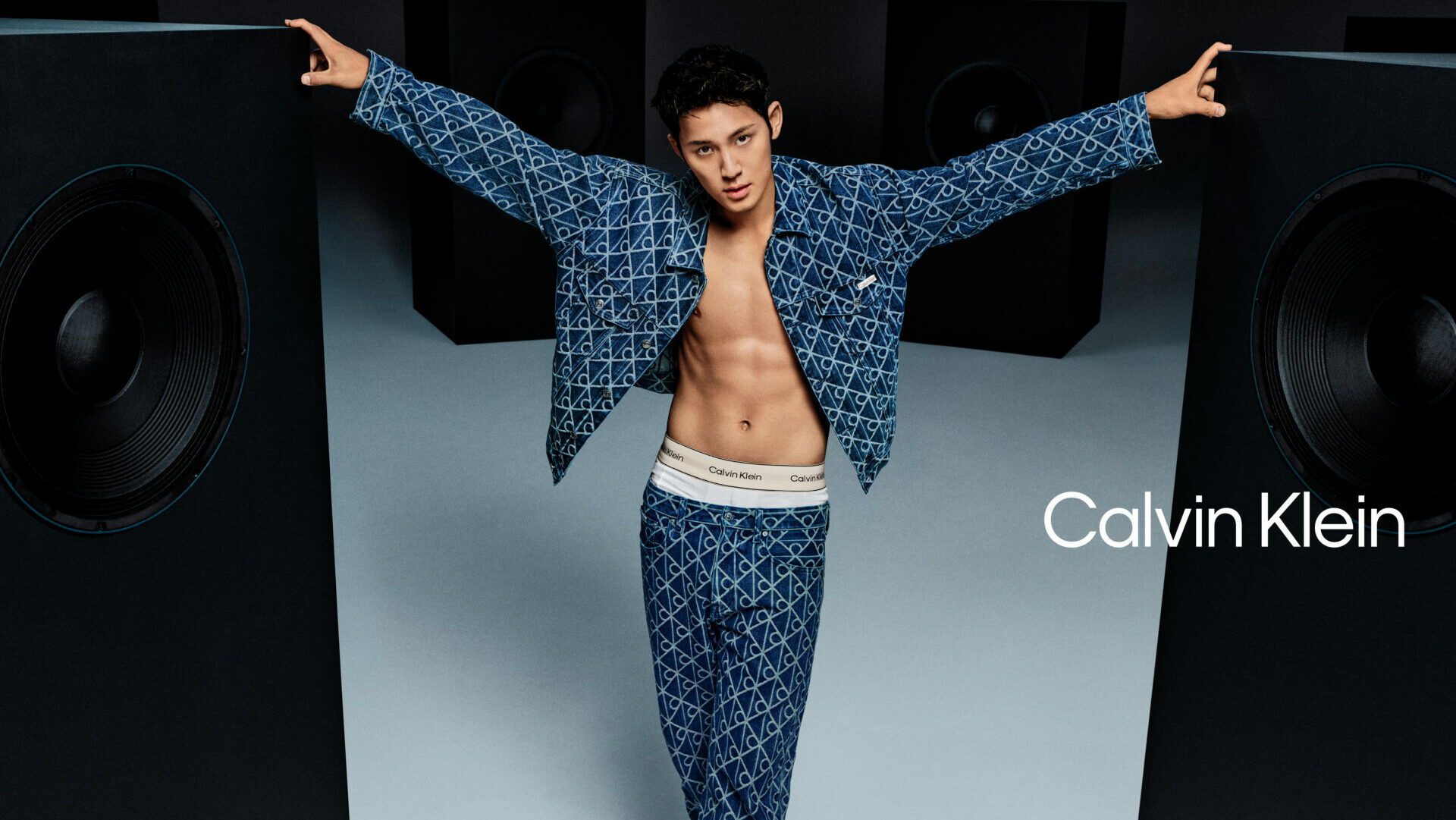 K-Pop star Mingyu stands in a studio wearing a Calvin Klein denim set, revealing his Calvin Klein logo waistband underwear.