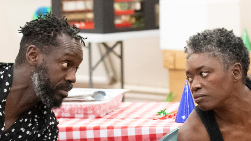 Two cast members in an intense rehearsal moment for Fat Ham, seated at a table