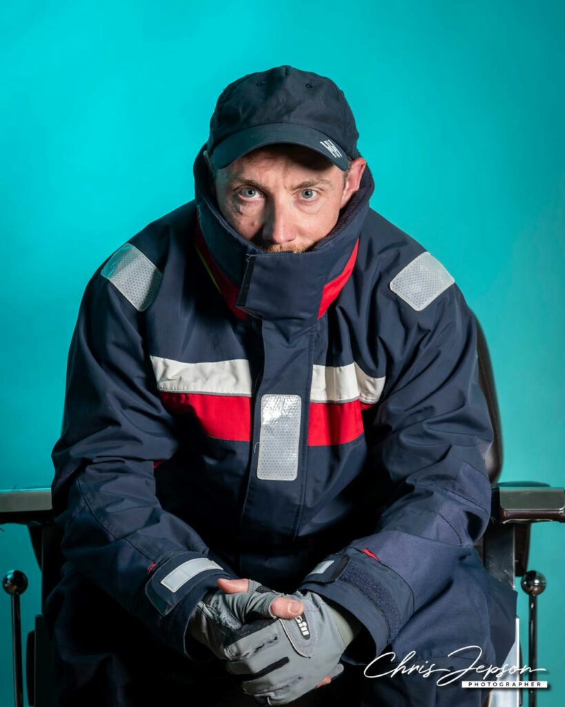 A person wearing skiing jacket and a cap sitting in a barber's chair