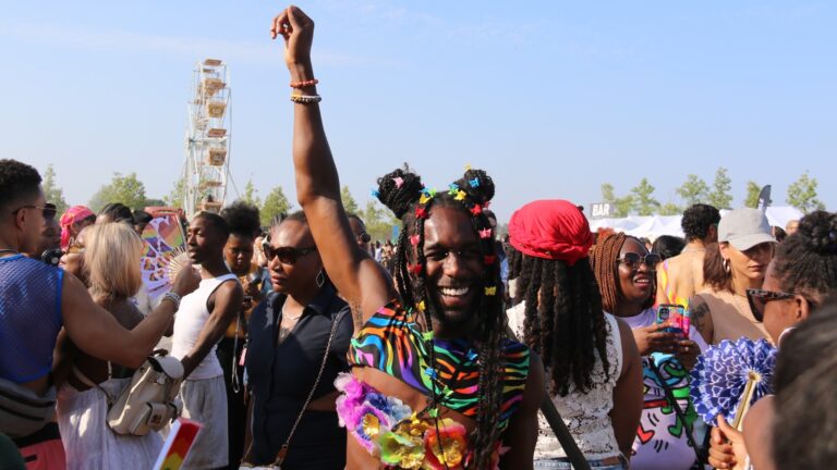 Man at UK Black pride 2025 with his arm stretched in the air wearing a rainbow outfit