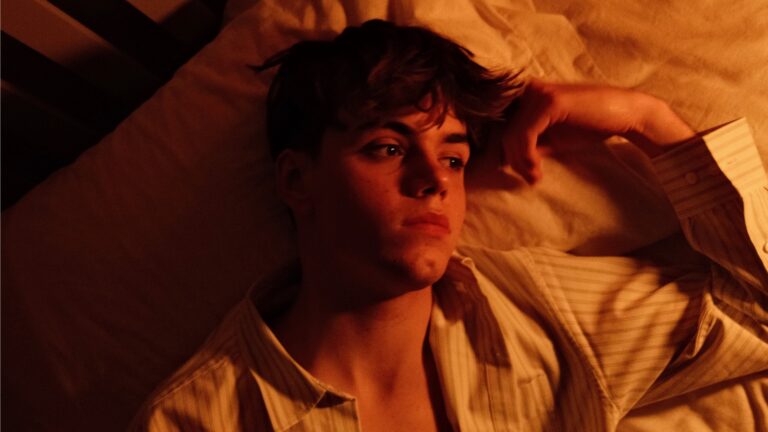 Fred Roberts in warm lighting laying on his bed with an open shirt