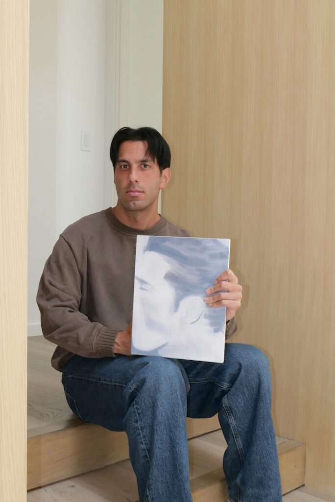 Jwan Yosef sitting and holding a copy of his book, in a brown top and blue jeans