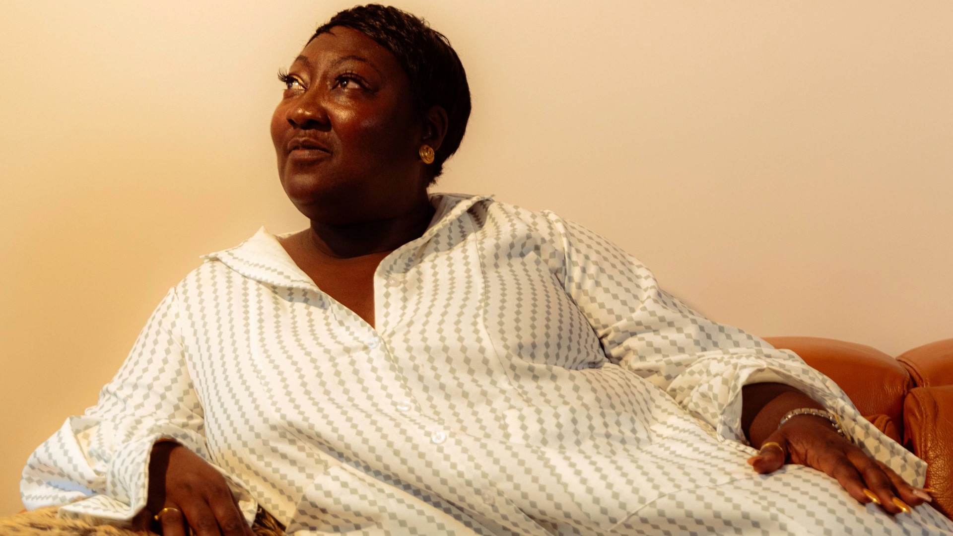 Lady Phyll reclining on a sofa looking away from the camera, wearing a white dress