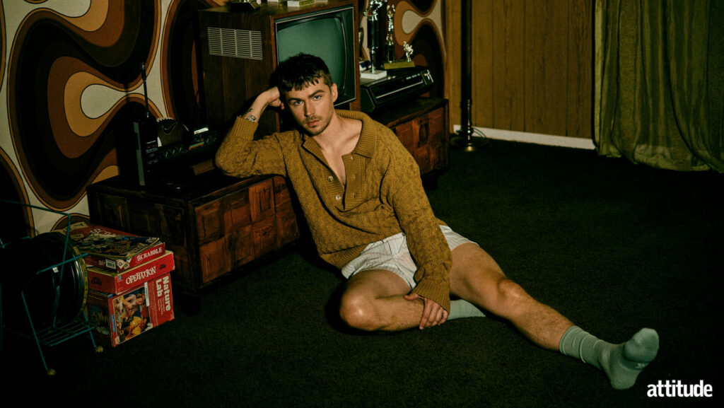 Miles Heizer in his Attitude cover shoot sitting on the floor in a darkly lit apartment