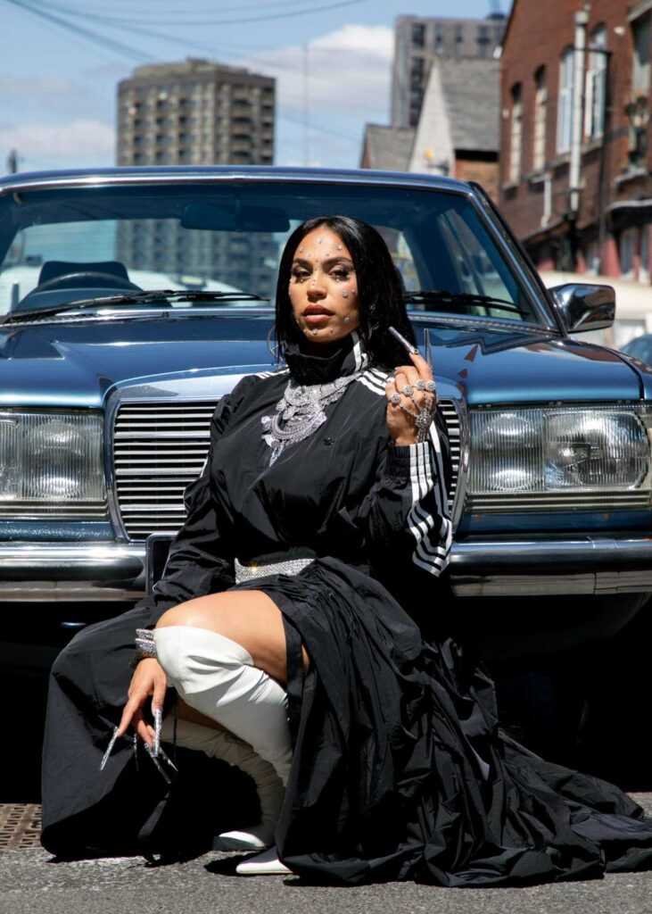 BombayMami wearing black posing in front of a black car