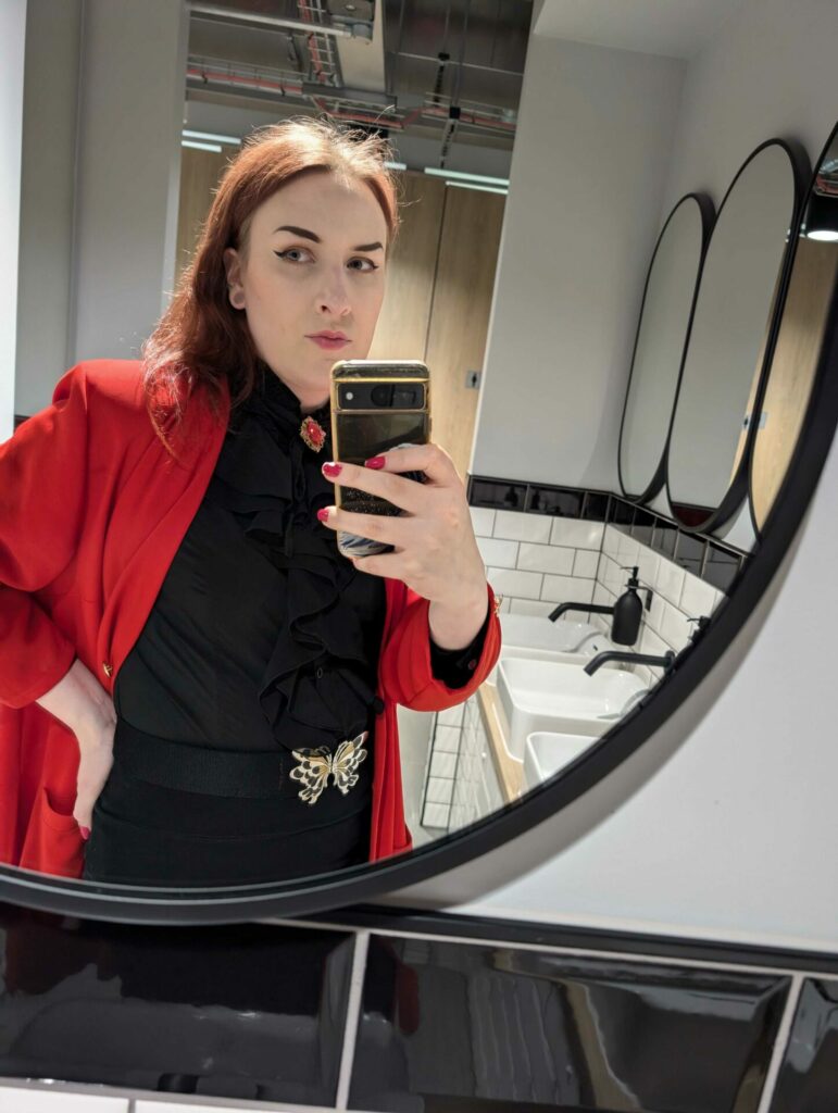 A woman in red and black taking a bathroom mirror selfie