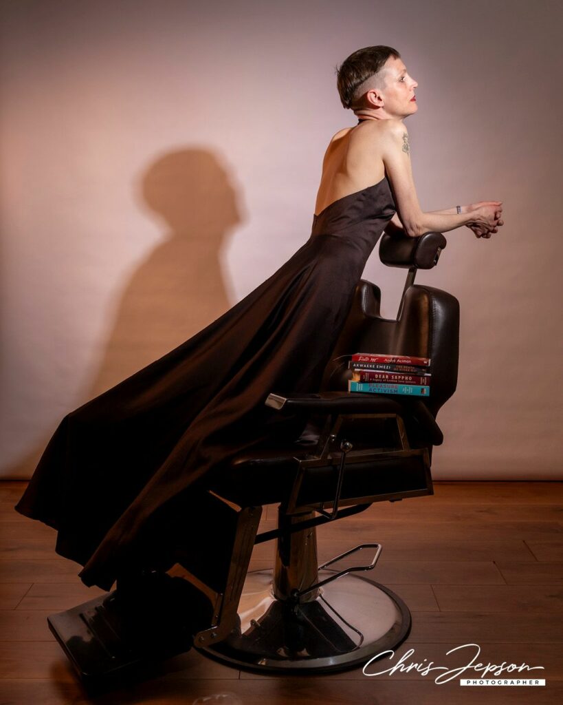 A person wearing a flowing black gown sitting across a barber's chair