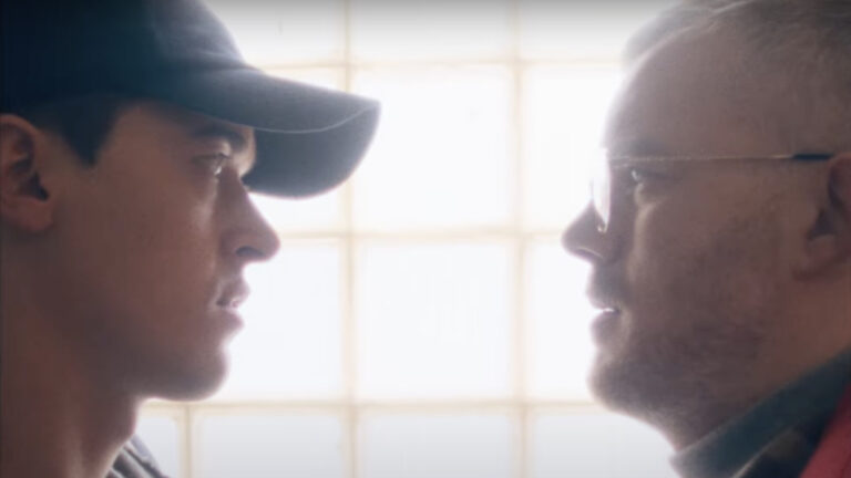 Tom Blyth and Russell Tovey stand face to face in public toilet