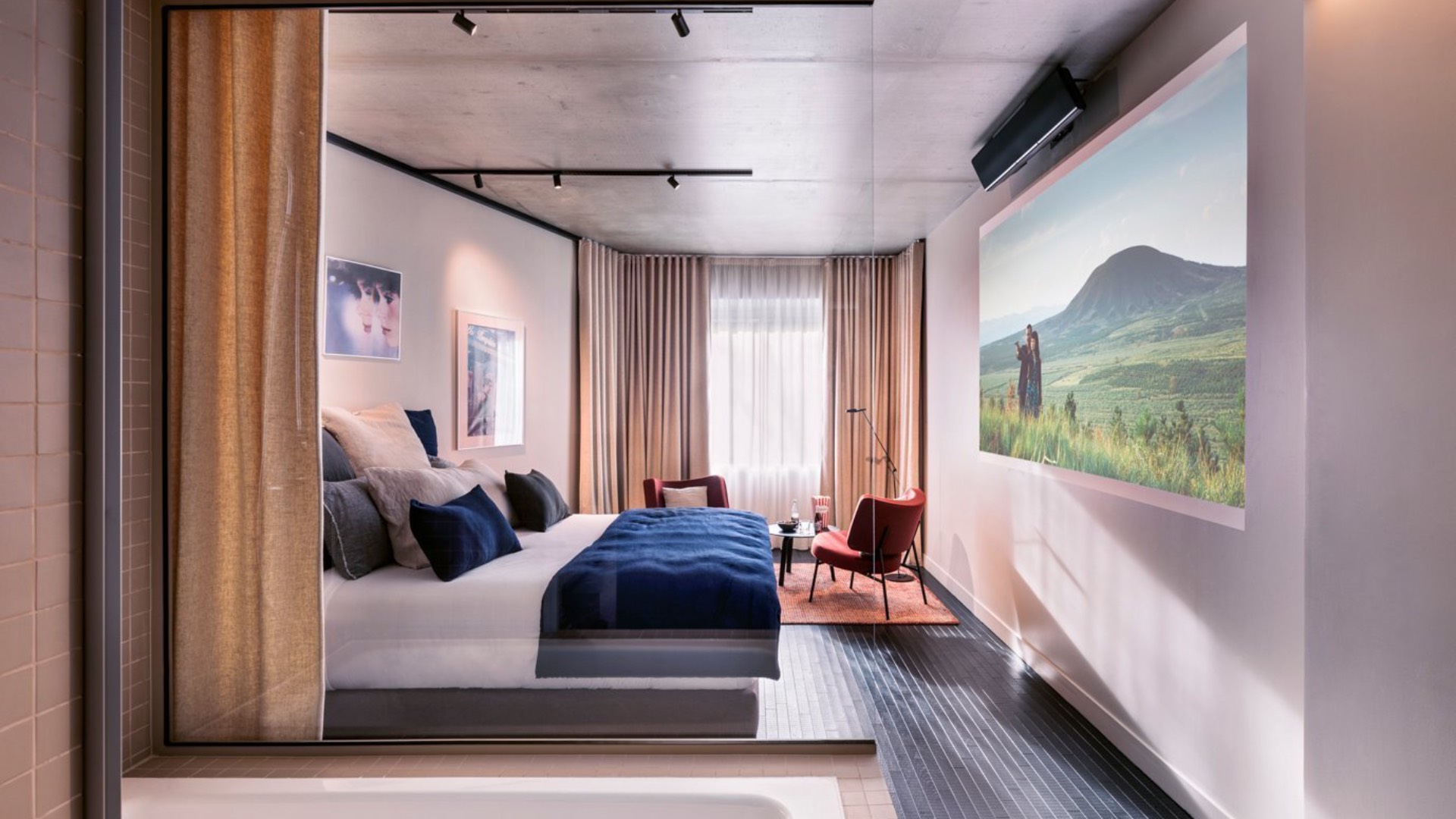a shot of one of the rooms of the hotel, featuring a bath, bed and projector with screen